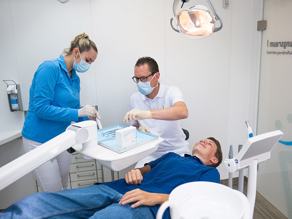 Behandlungsszene Dr. Plöger, Assistenz und junger Patient.